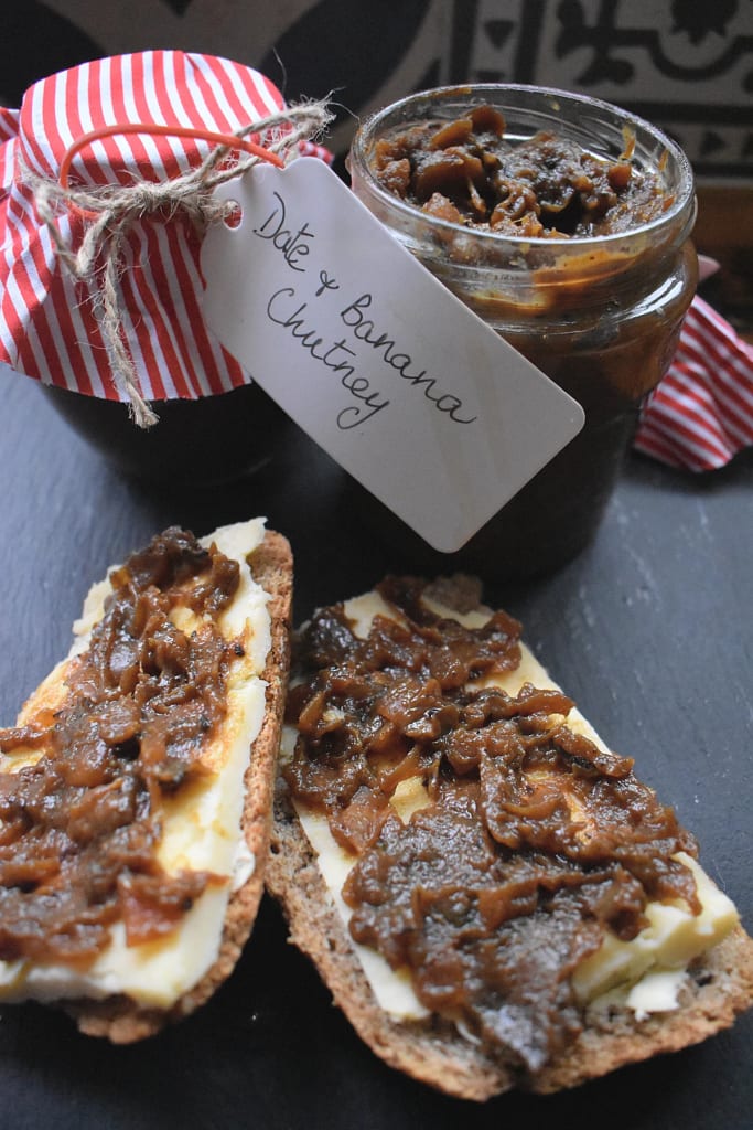 Date and Banana Chutney spread on two slices of bread and cheese with jars of the chutney in the background.